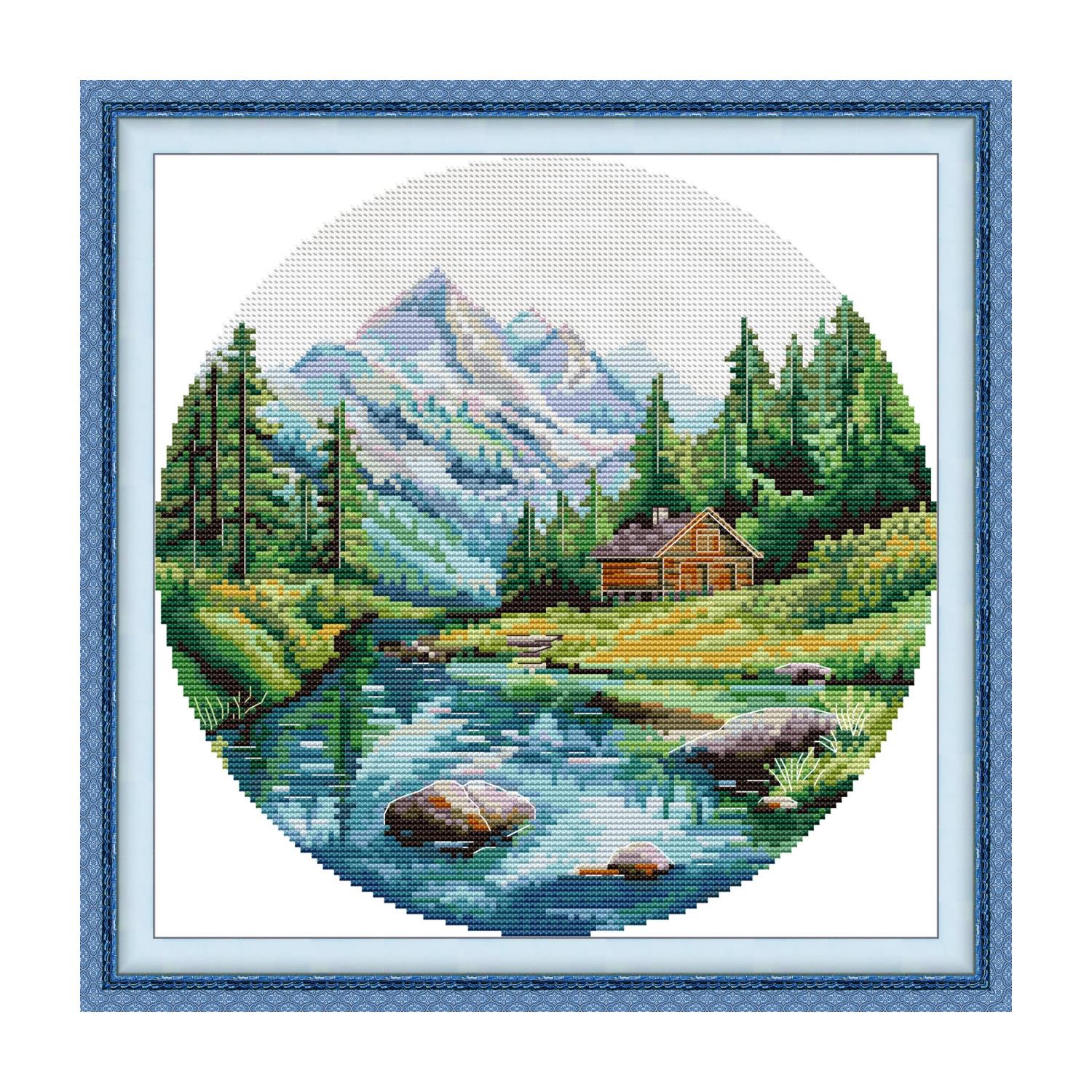 Landscape cross stitch design of a summer mountain lake with a log cabin and pine forest, in a round composition