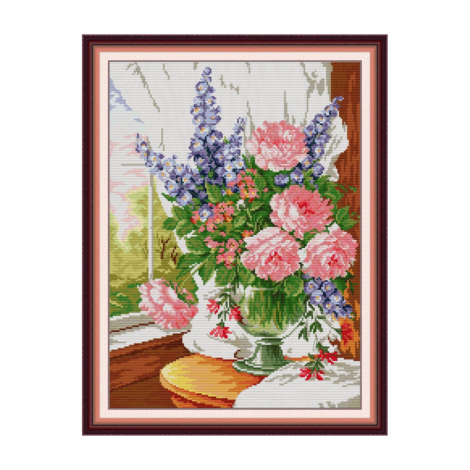 Floral cross stitch design of pink roses and purple larkspur in a white vase on a windowsill